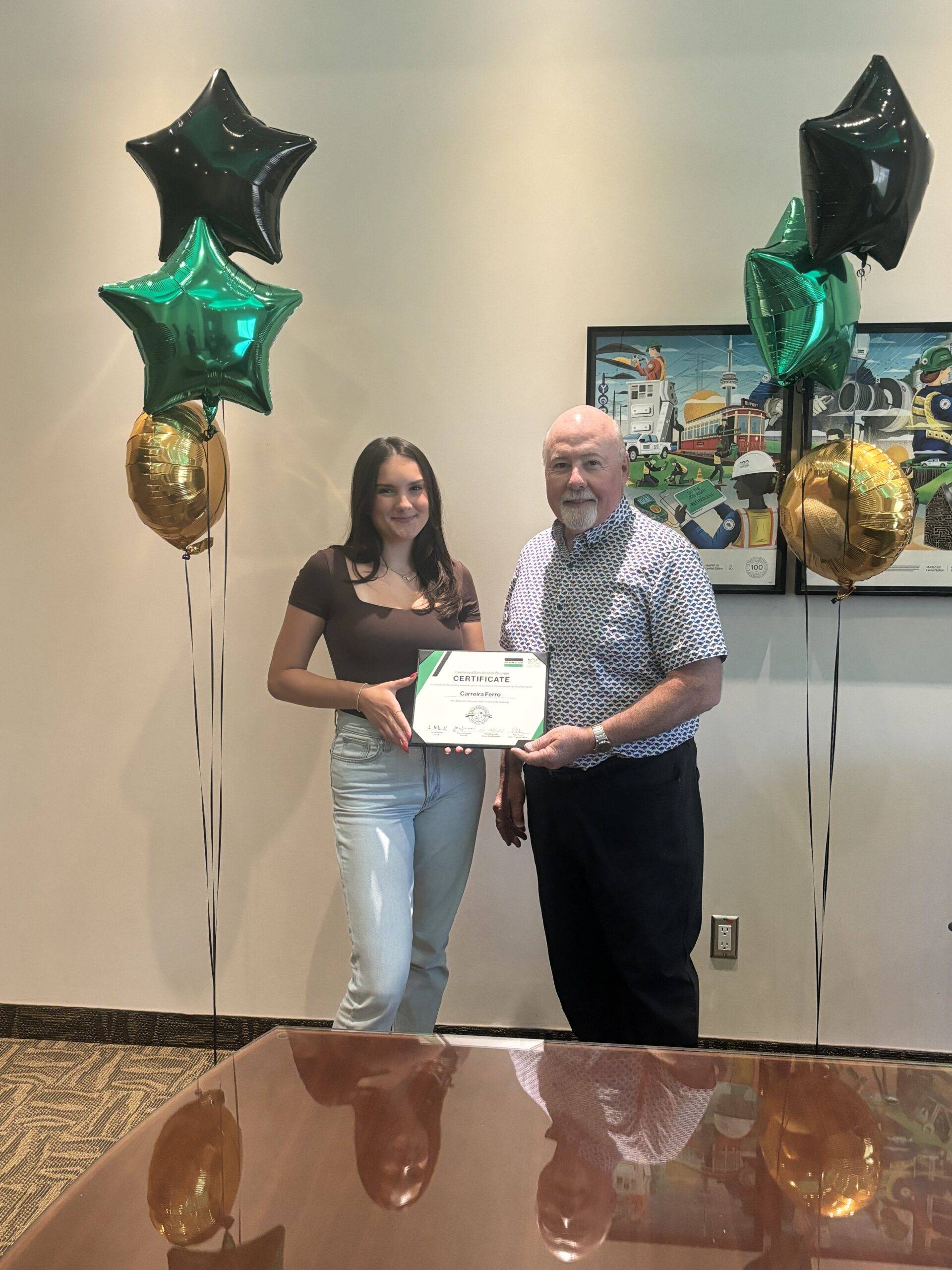 A scholarship recipient, and her father hold a certificate commemorating the Centennial Scholarships.