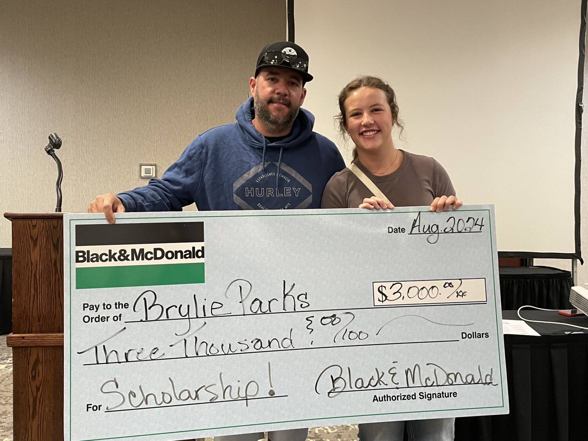 A scholarship recipient and her father receive a large novelty cheque